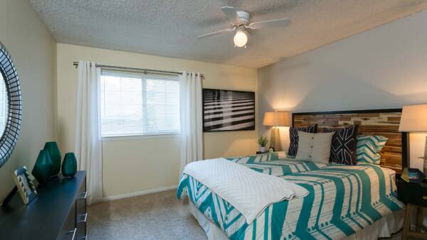 Bedroom with carpet, bed with wood headboard, ceiling fan, and large window.