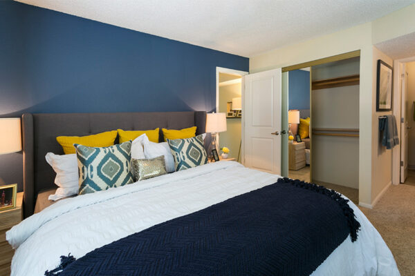 Bedroom with carpet, bed with plush headboard, blue accent wall, and closet with mirror door.
