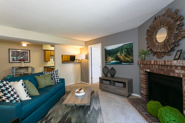 Living room with carpet, plush couch, modern wood furniture, and brick fireplace.