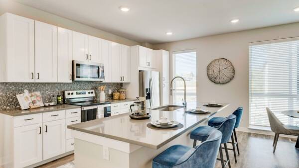 Kitchen with wood floor, white cabinets, tan counters, tiled backsplash, and breakfast bar.