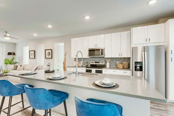 Kitchen with white cabinets, tan counters, stainless steel appliances, and island with stools.