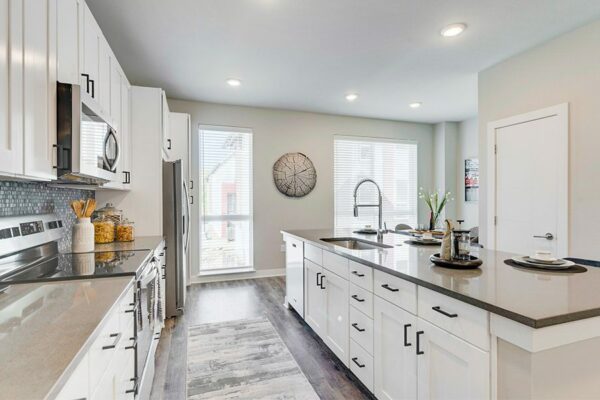 Kitchen with floor runner, white cabinets, tan counters, stainless steel appliances, and large windows.