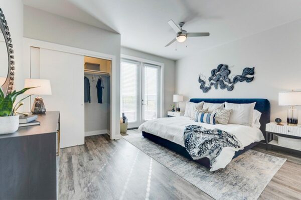 Bedroom with wood floor, large bed with plush headboard, large closet, and door to balcony.