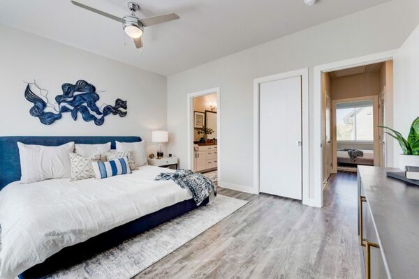Bedroom with wood floor, large bed with plush headboard, bedside tables with lamps, and doors to closet, bathroom, and hallway.