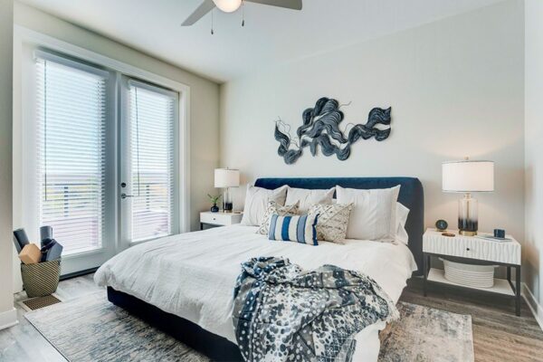 Bedroom with large bed with plush headboard, bedside tables with lamps, and door to balcony.