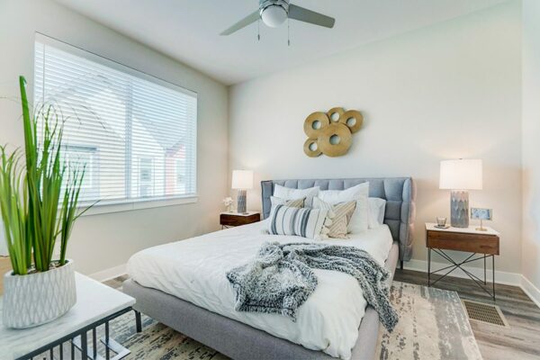 Bedroom with large bed with plush headboard, modern furniture and artwork, ceiling fan, and large window.