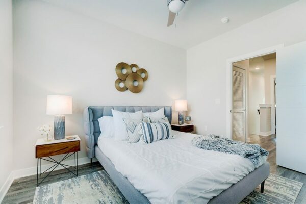 Bedroom with large bed with plush headboard, bedside tables with lamps, ceiling fan, and door to hallway.