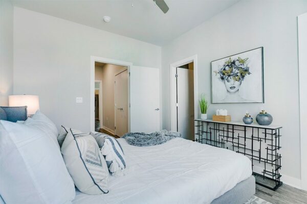 Bedroom with large bed with plush headboard, modern furniture and artwork, and doors to hallway and bathroom.
