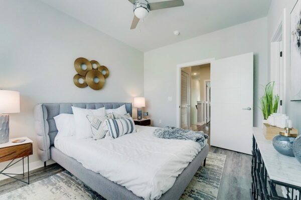 Bedroom with large bed with plush headboard, modern furniture and artwork, ceiling fan, and door to hallway.