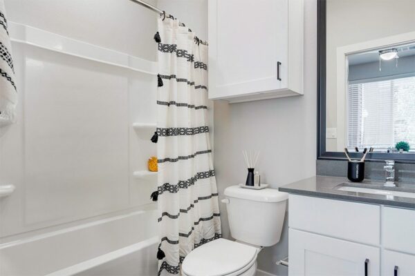 Bathroom with white cabinets, grey counters, large framed mirror, and shower tub with curtain.