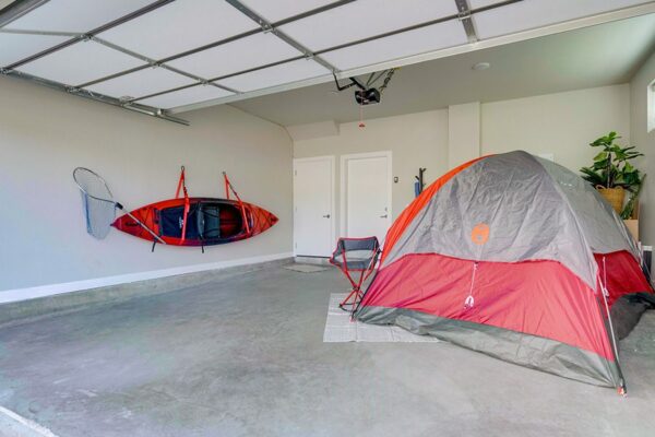 Garage with tent and camping chairs set up and kayak attached to wall.