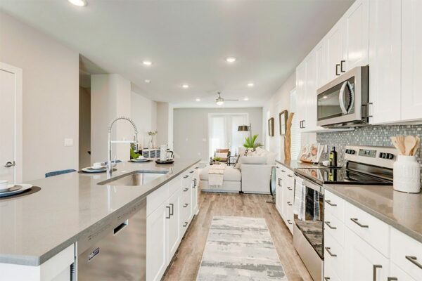 Kitchen with wood floor, white cabinets, tan counters, and stainless steel appliances.