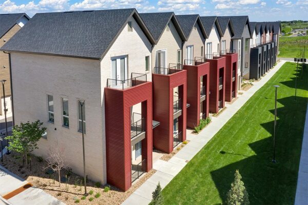 Aerial view of Dayton Station townhomes with red siding and balconies overlooking lush lawn.
