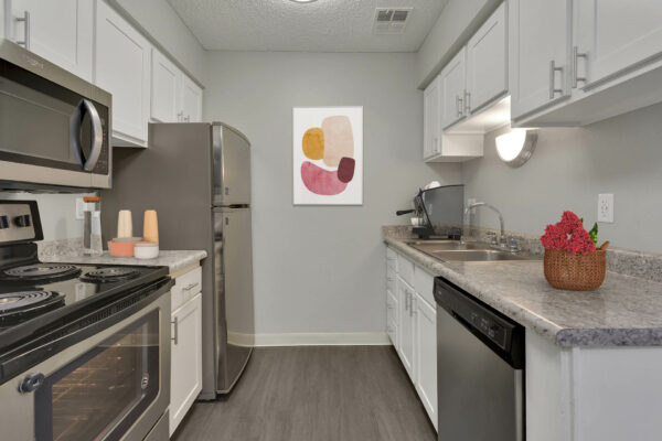 Kitchen with wood floor, white cabinets, stainless steel appliances, and artwork.