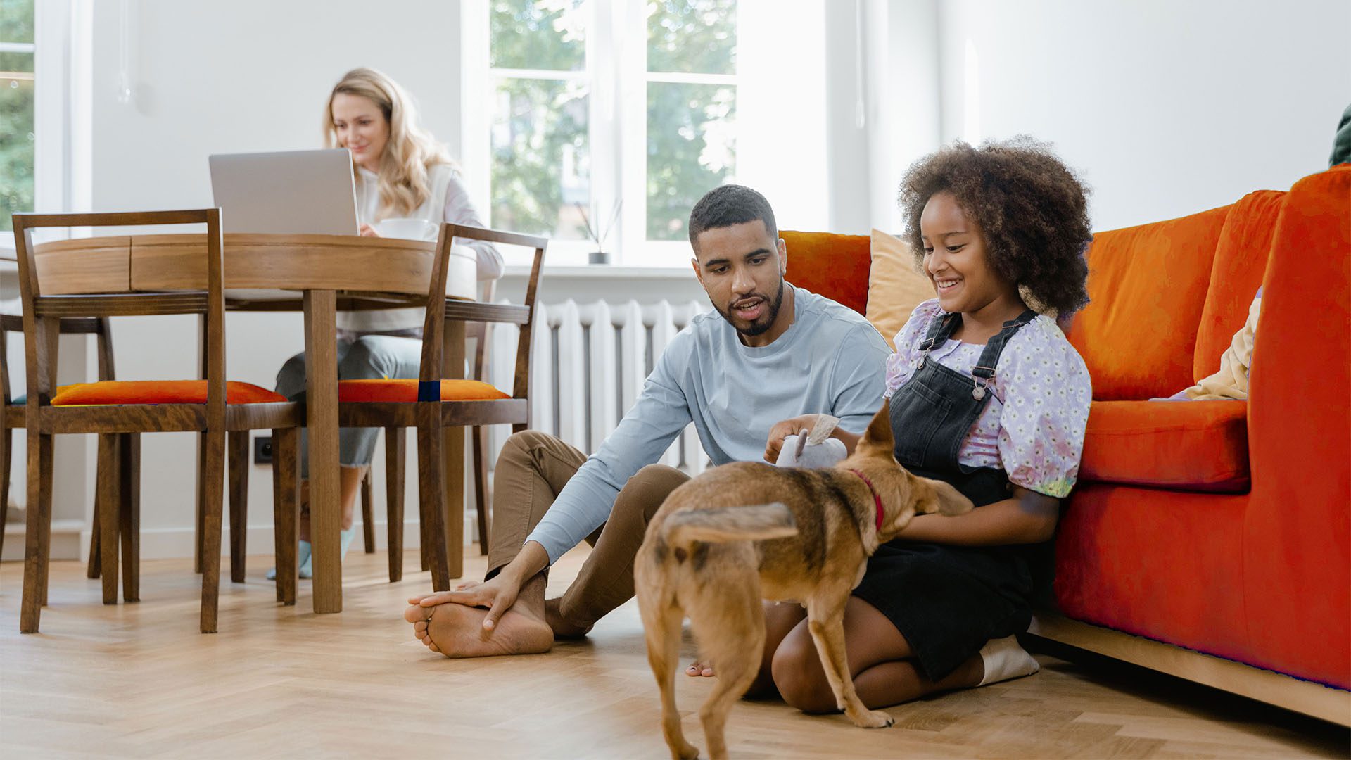 Family with dog in living room with wood floor and plush orange couch.
