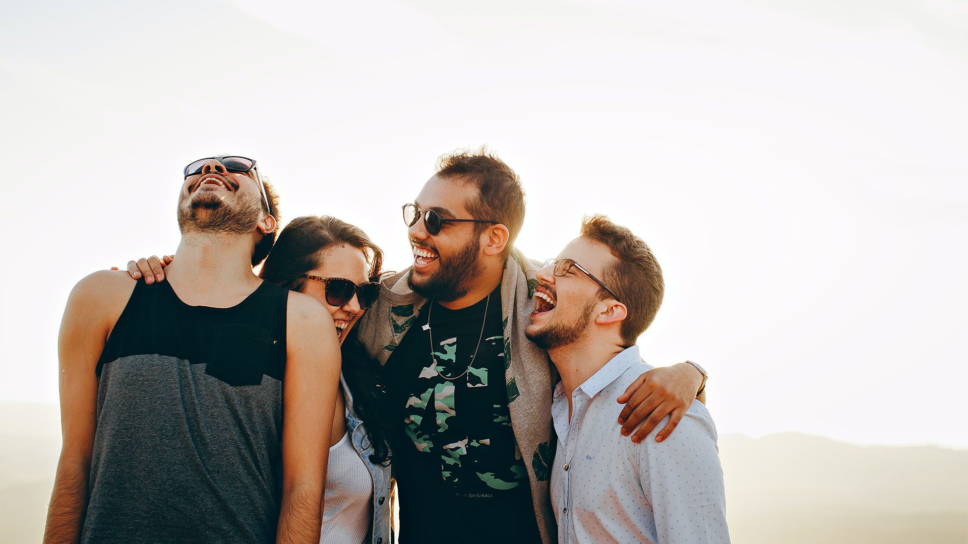 Friends laughing outside with arms around each other.