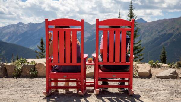 Friends sitting on mountaintop in large red wood chairs.