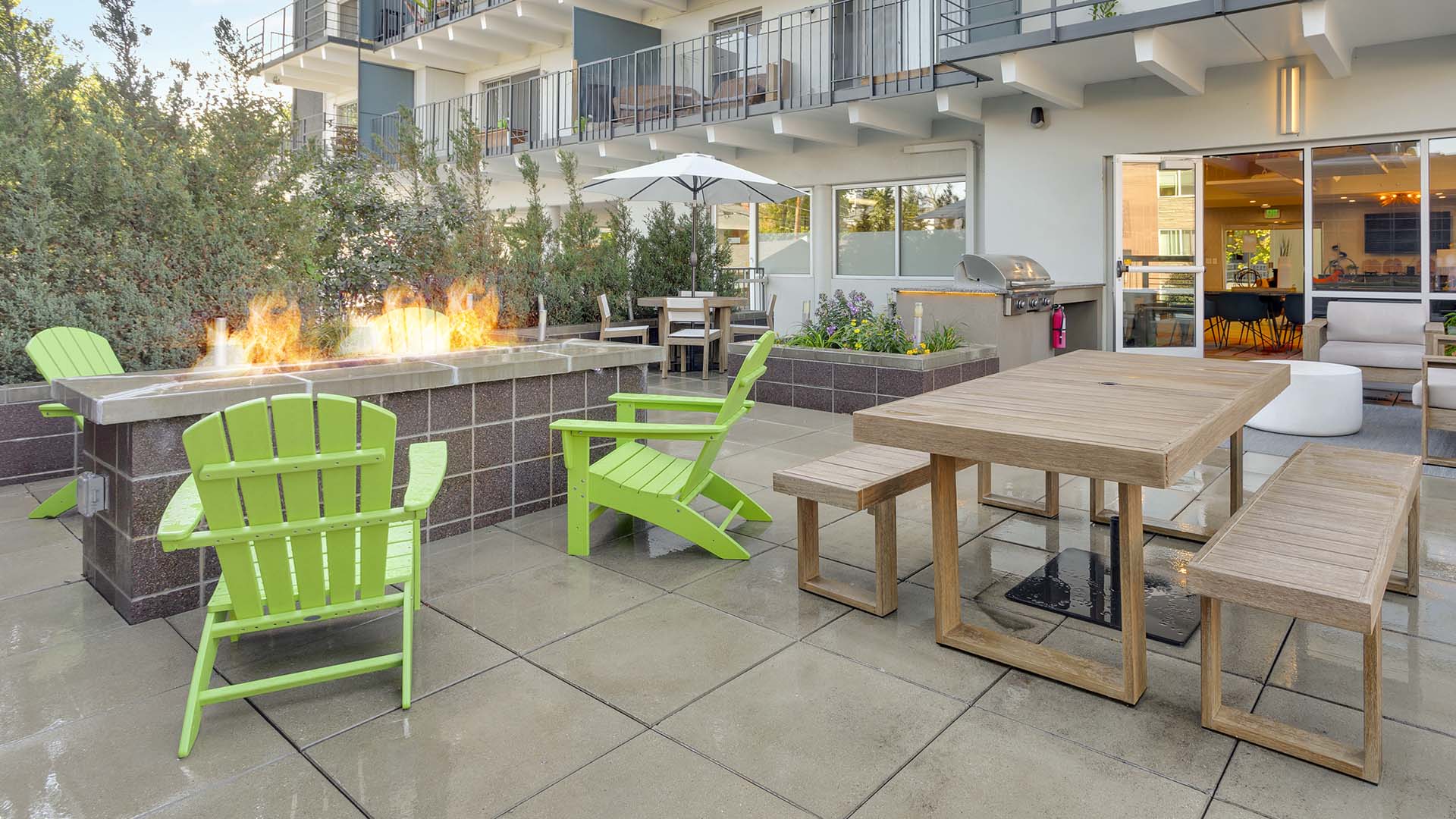 Patio with picnic tables, lounge chairs, BBQ and fire pit overlooked by apartment balconies.