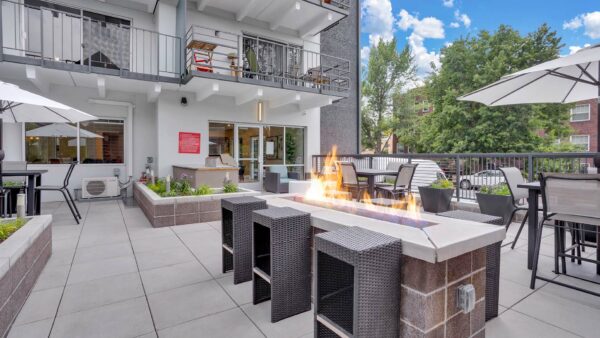 Patio with picnic tables, lounge chairs, BBQ and fire pit overlooked by apartment balconies.
