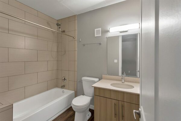 Bathroom with wood floor and cabinet, light counter, large mirror, and tiled shower tub.