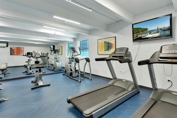 Fitness center with mirror wall, wall mounted TV, treadmills, elliptical, and exercise bike.