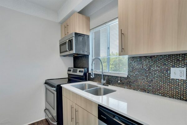Kitchen with wood cabinets, light counters, stainless steel appliances and sink, and round tiled backsplash.