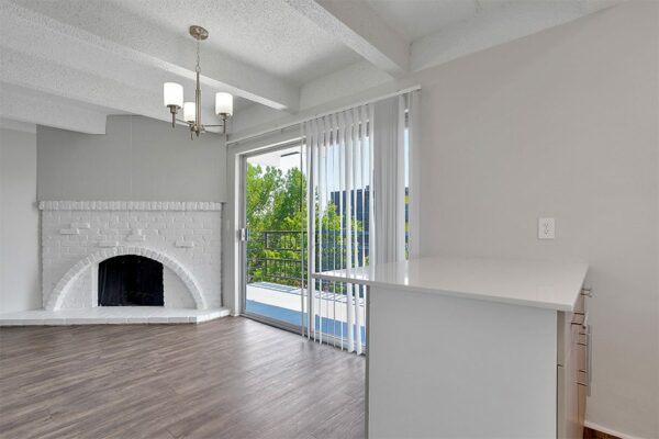 Living area with wood floor, kitchen island, white brick fireplace, and door to balcony.