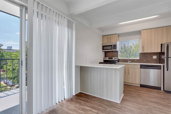 Living area with wood floor, kitchen with island, and sliding door to balcony.