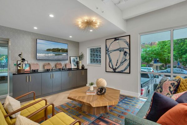 Lounge with patterned rug, comfortable modern furniture, wall mounted TV, and abstract artwork.