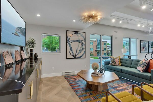 Lounge with patterned rug, comfortable modern furniture, wall mounted TV, and abstract artwork.