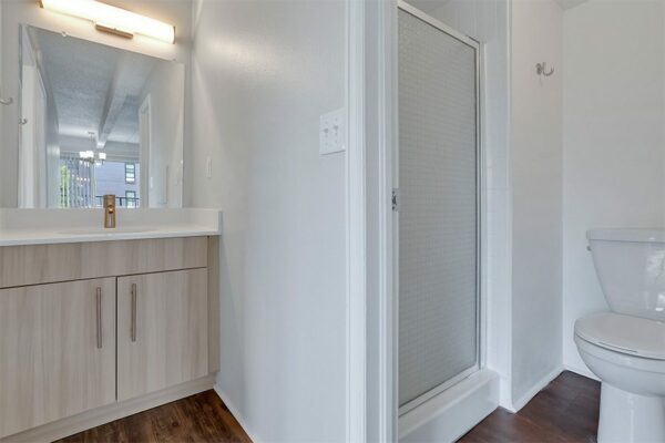 Bathroom with wood cabinet, white counters, large mirror, and frosted glass shower door.