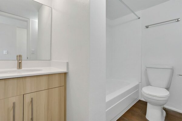 Bathroom with wood floor and cabinets, white counter and sink, large mirror, and tiled shower tub.