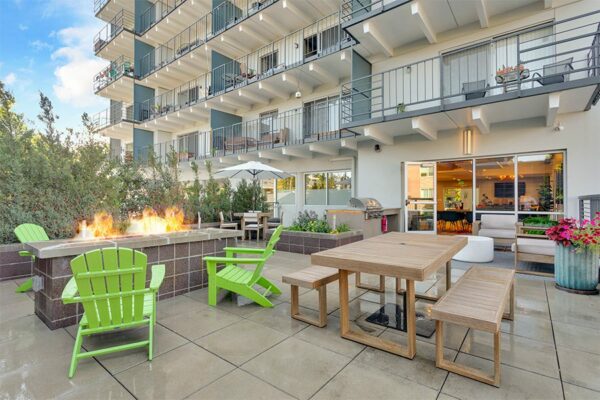 Patio with outdoor furniture, fire pit, and built in BBQ grill overlooked by apartment balconies.