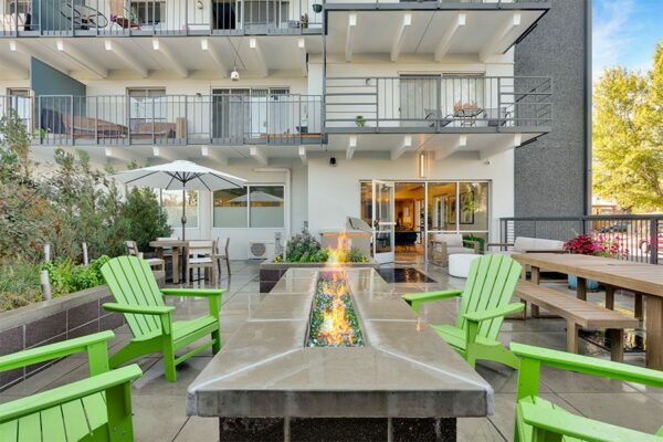 Patio with outdoor furniture, fire pit, and built in BBQ grill overlooked by apartment balconies.