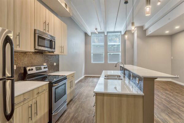 Living room with wood floor and cabinets, light counters, stainless steel appliances, and modern pendant lights.