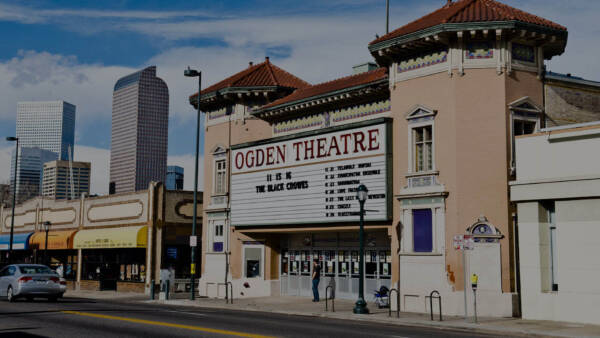 Ogden Theatre on Colfax in Denver with classic construction, large marquee sign, and Denver skyline behind.