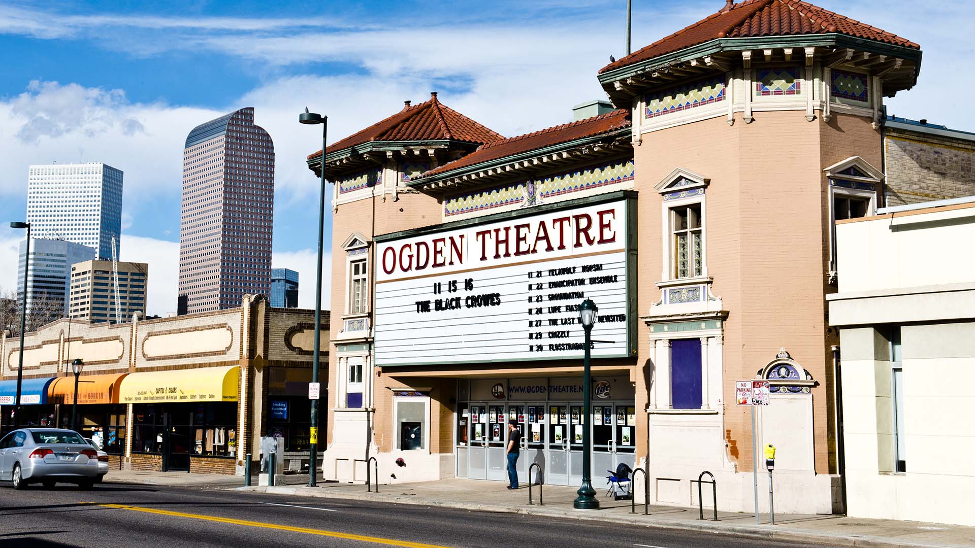 Ogden Theatre on Colfax in Denver with classic construction, large marquee sign, and Denver skyline behind.