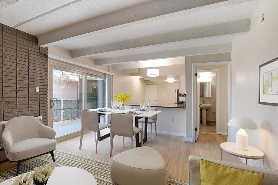 Living room with wood floor, modern furniture, brick accent wall, dining set, and door to balcony.