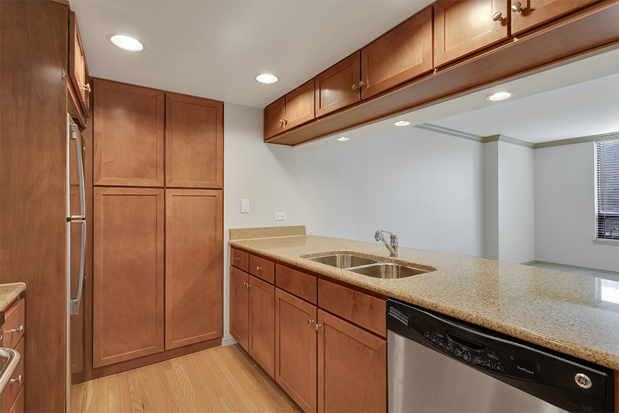 Apartment kitchen with wood floor and cabinets, stone counters, and stainless steel appliances.