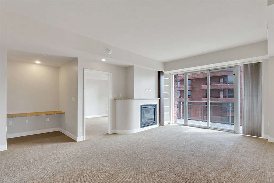 Apartment living room with carpet, built in desk, fireplace, and large door to balcony.