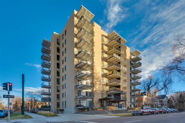 Story apartments with blonde brick construction, large balconies, garage entrance, and ample parking.