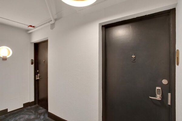 Hallway with pattern carpet, white walls, and metal doors to apartments.