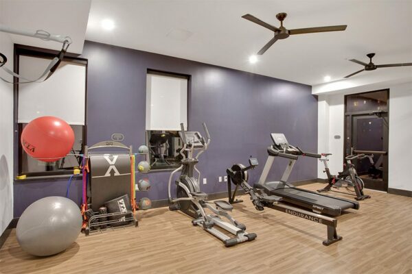 Fitness center with wood floor, large ceiling fans, calisthenics equipment, and cardio machines.