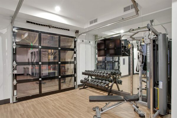 Fitness center with wood floor, dumbbell rack, weight machine, and garage door to outside.
