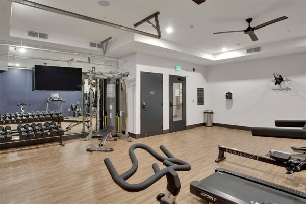 Fitness center with wood floor, dumbbell rack, weight machine, cardio machines, and wall mounted TV.