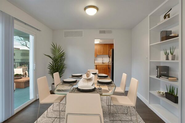 Dining room with wood floor, modern glass dining table with chairs, bookshelf with decor, and sliding door to balcony.
