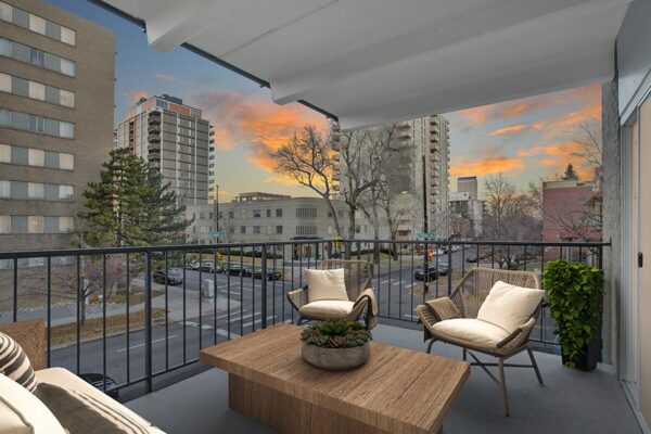 Balcony with metal railing, wicker chairs, and outdoor table with potted plant overlooking street.