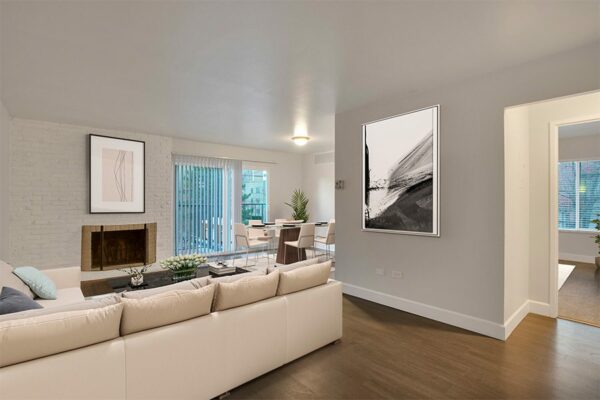 Living room with wood floor, white leather sectional, brick accent wall with fireplace, and sliding door to balcony.