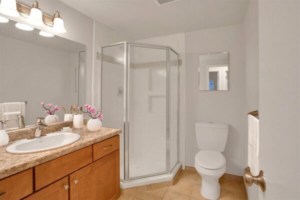 Bathroom with tile floor, wood cabinets, stone counter, large mirror with light fixture, and glass wall shower.