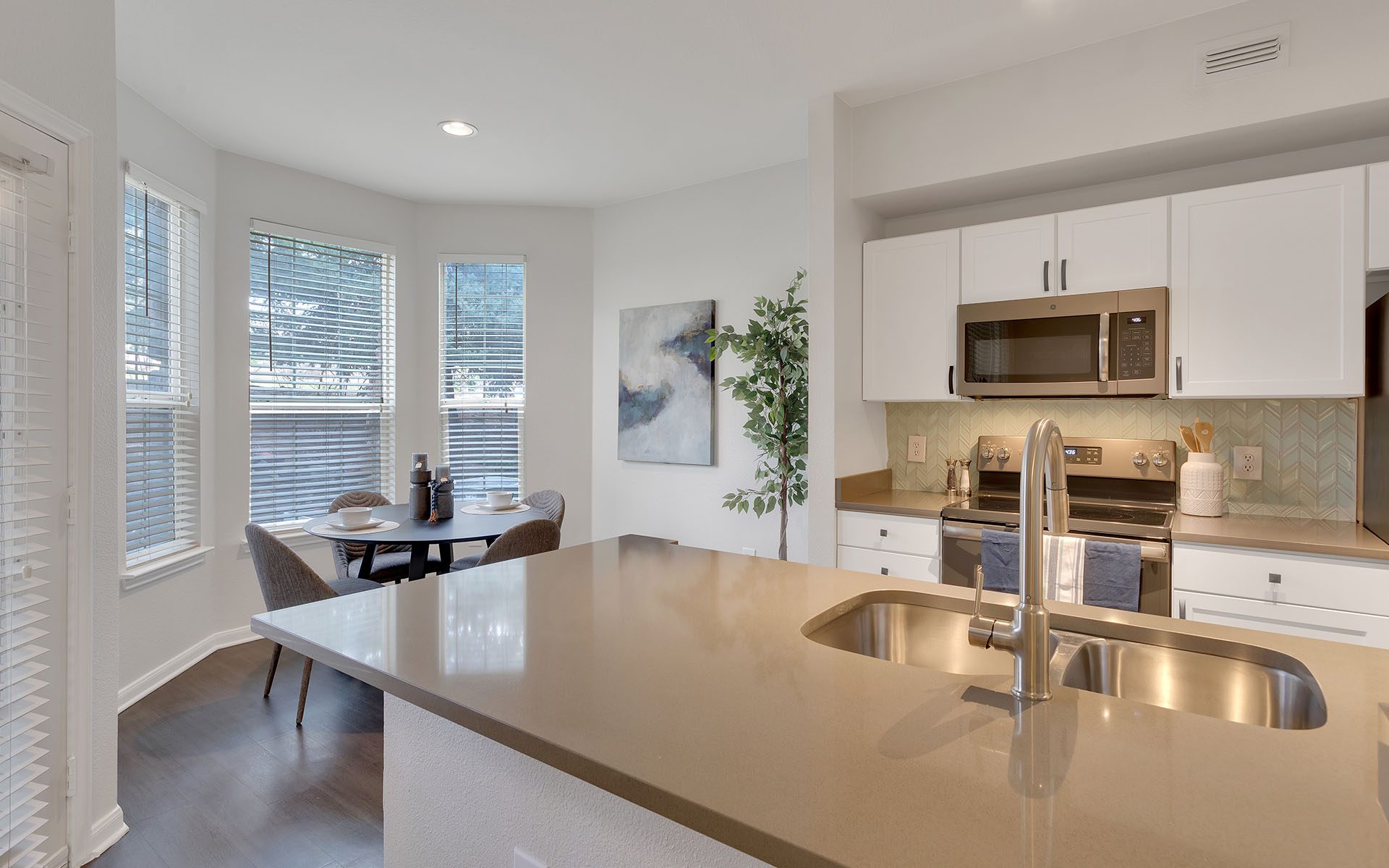 Dining room connected to living area and kitchen with wood floor and white walls.